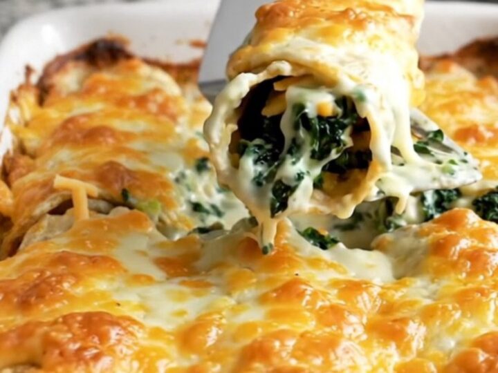 A top-down view of a rectangular ceramic baking dish filled with spinach and cheese enchiladas covered in white sauce.