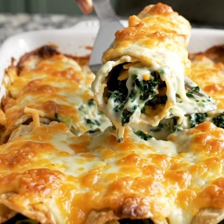 A top-down view of a rectangular ceramic baking dish filled with spinach and cheese enchiladas covered in white sauce.