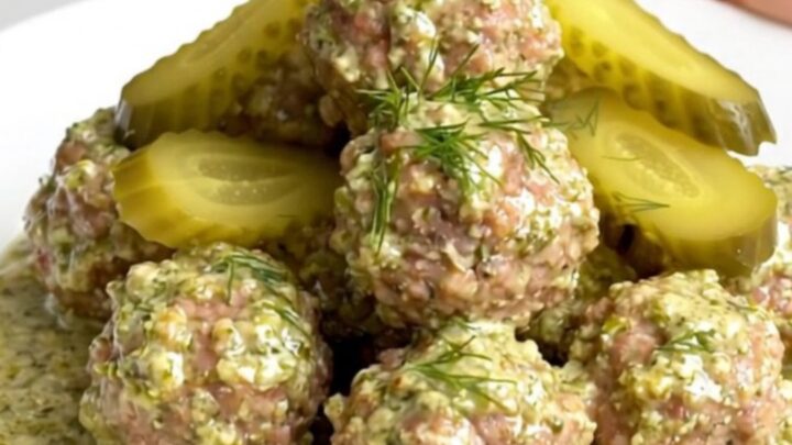 A close-up of tender beef meatballs covered in a rich, creamy dill pickle sauce served on a white plate.