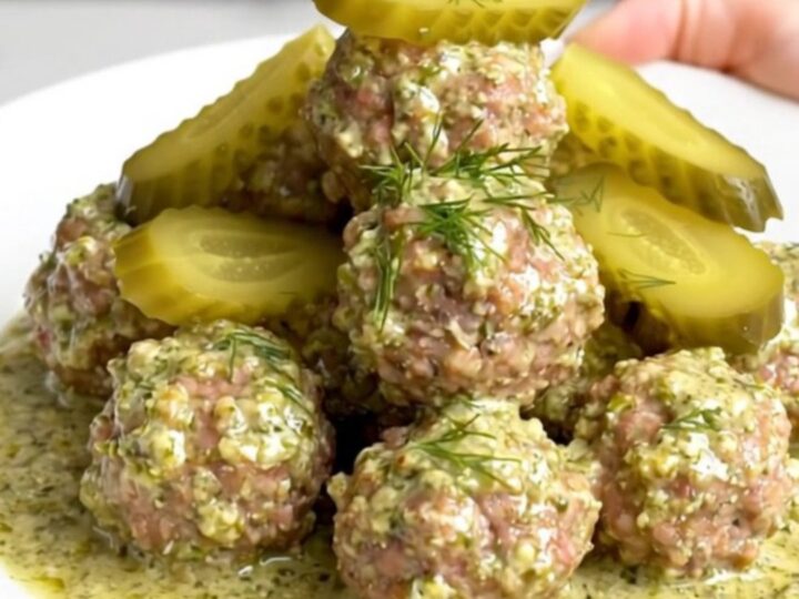 A close-up of tender beef meatballs covered in a rich, creamy dill pickle sauce served on a white plate.