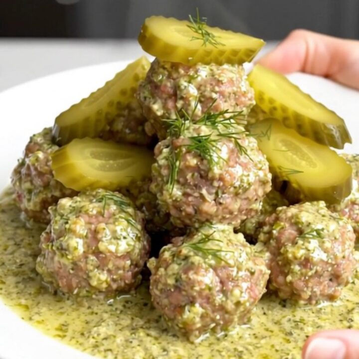 A close-up of tender beef meatballs covered in a rich, creamy dill pickle sauce served on a white plate.