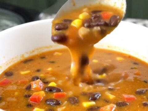 A close-up of creamy black bean salsa soup in a black slow cooker, showing beans, corn, and peppers.