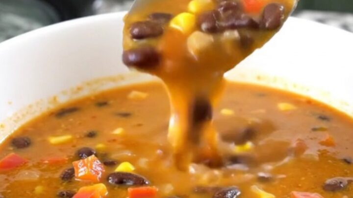 A close-up of creamy black bean salsa soup in a black slow cooker, showing beans, corn, and peppers.