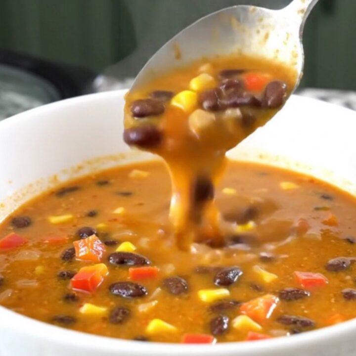 A close-up of creamy black bean salsa soup in a black slow cooker, showing beans, corn, and peppers.