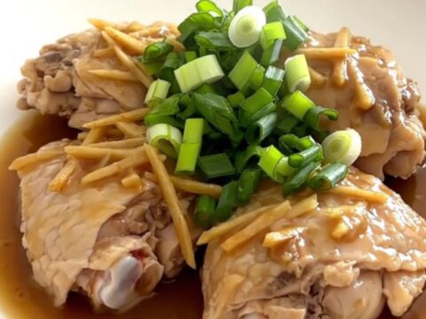 Tender chicken thighs in a savory ginger scallion sauce served on a white plate.