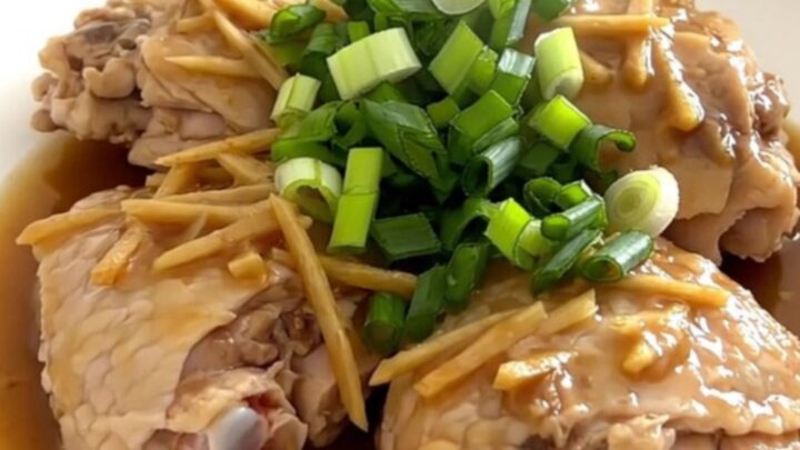Tender chicken thighs in a savory ginger scallion sauce served on a white plate.