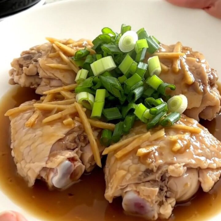 Tender chicken thighs in a savory ginger scallion sauce served on a white plate.