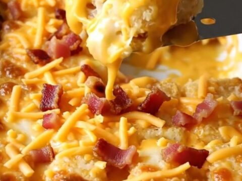 A top-down view of a rectangular ceramic dish filled with crispy potato tots covered in beer cheese, cheddar, and bacon.