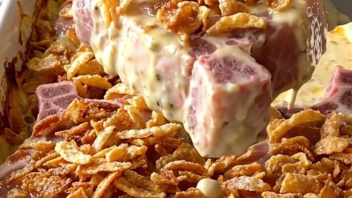 A rectangular ceramic dish filled with baked, creamy pork chops topped with crispy golden onions.