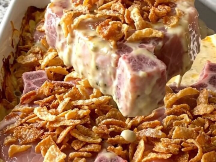 A rectangular ceramic dish filled with baked, creamy pork chops topped with crispy golden onions.