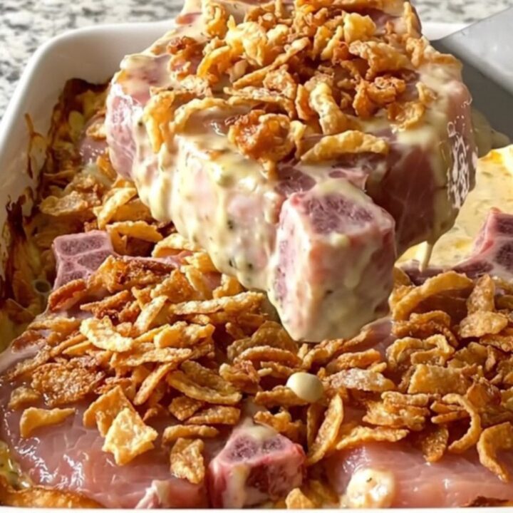 A rectangular ceramic dish filled with baked, creamy pork chops topped with crispy golden onions.