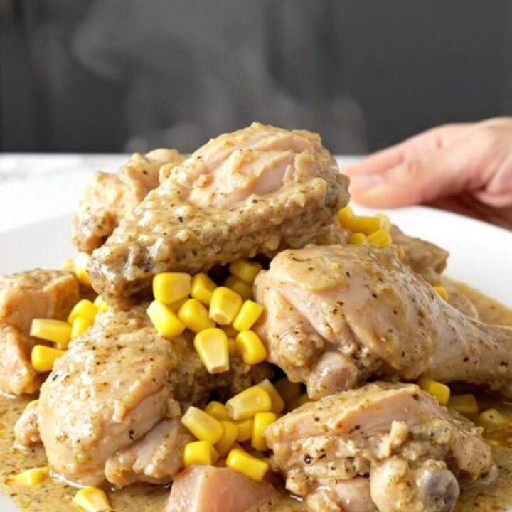 A close-up of tender chicken pieces and corn kernels coated in a thick, creamy peppered gravy, served on a white plate.