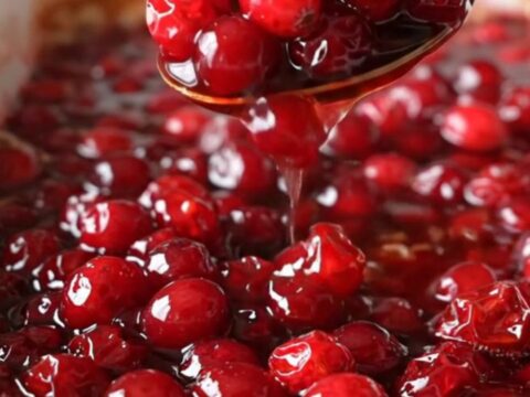 A ceramic dish filled with vibrant, baked red cranberries in a glossy, thick maple cinnamon sauce.