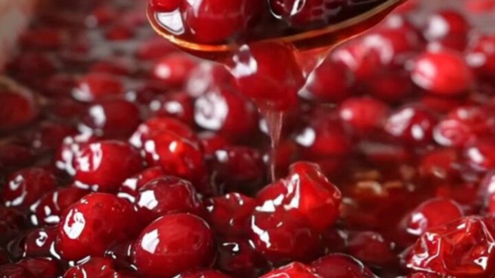 A ceramic dish filled with vibrant, baked red cranberries in a glossy, thick maple cinnamon sauce.