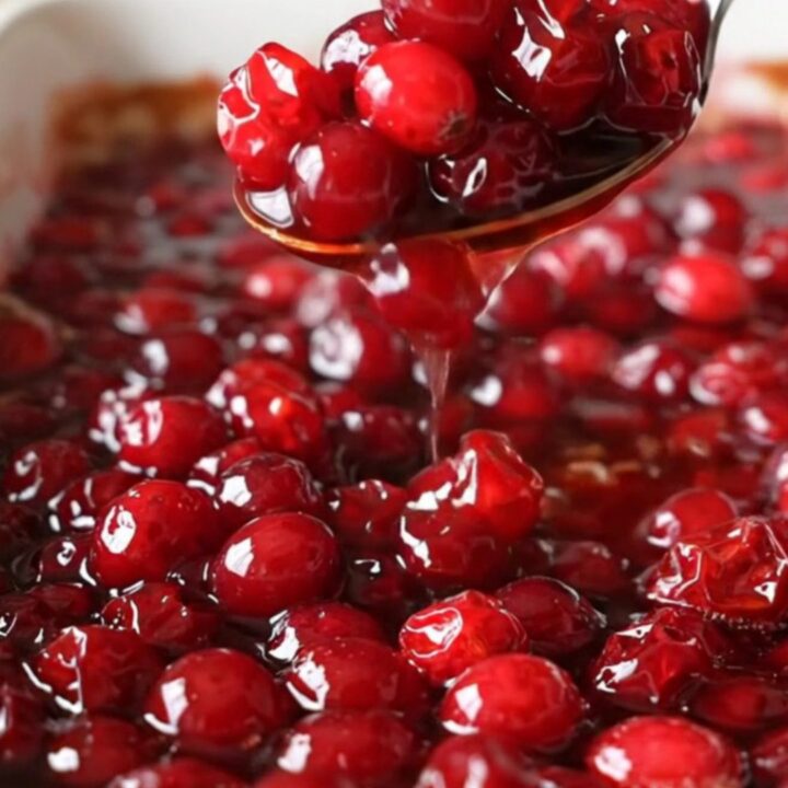 A ceramic dish filled with vibrant, baked red cranberries in a glossy, thick maple cinnamon sauce.