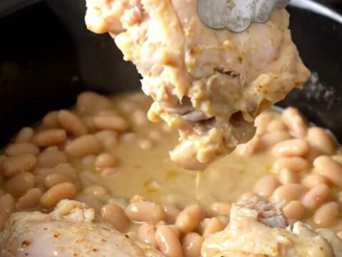 A rustic bowl of slow-cooked chicken thighs nestled among white beans in a savory rosemary sauce.