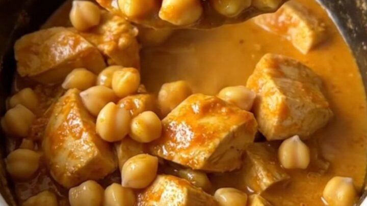 Slow cooker curried chicken and chickpeas in a white ceramic dish, steaming and topped with fresh herbs.