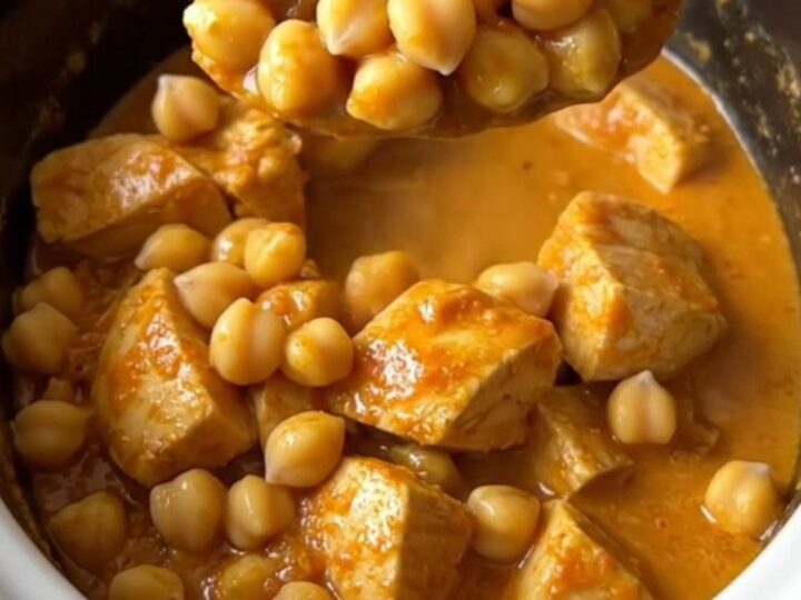 Slow cooker curried chicken and chickpeas in a white ceramic dish, steaming and topped with fresh herbs.