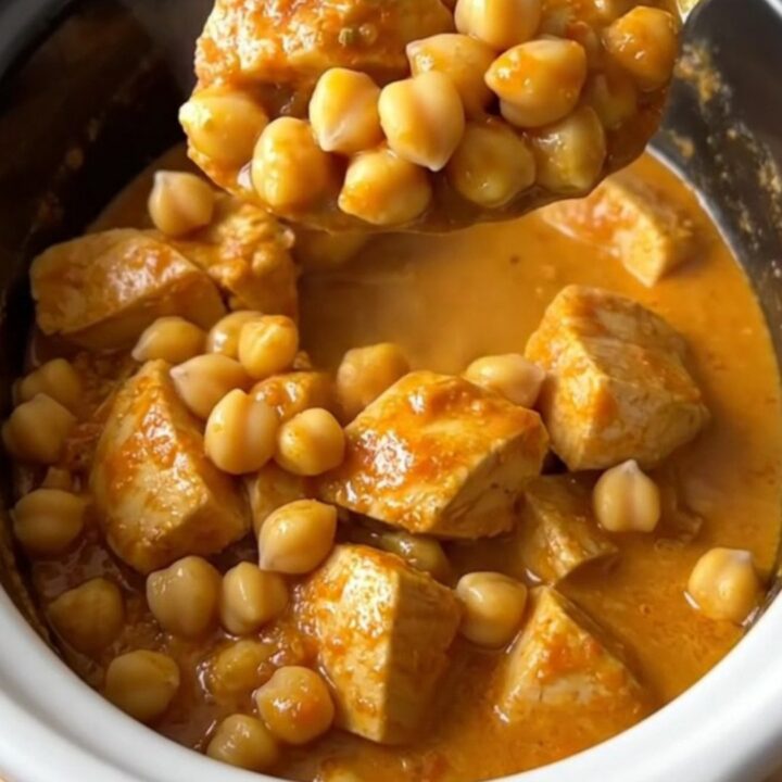 Slow cooker curried chicken and chickpeas in a white ceramic dish, steaming and topped with fresh herbs.