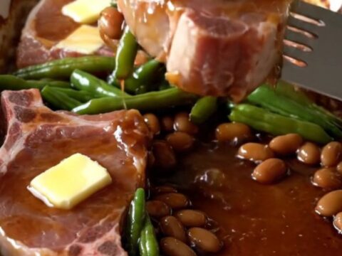 A top-down view of a rectangular baking dish filled with raw pork chops and green beans ready for the oven.