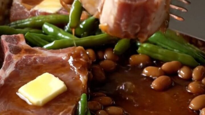 A top-down view of a rectangular baking dish filled with raw pork chops and green beans ready for the oven.