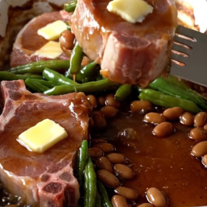 A top-down view of a rectangular baking dish filled with raw pork chops and green beans ready for the oven.