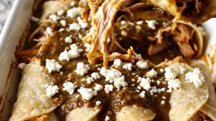 A rectangular ceramic baking dish filled with chicken mole enchiladas topped with crumbled white queso fresco.