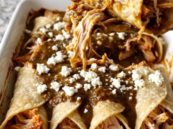 A rectangular ceramic baking dish filled with chicken mole enchiladas topped with crumbled white queso fresco.