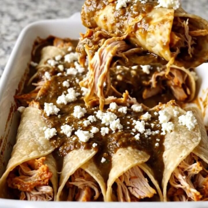 A rectangular ceramic baking dish filled with chicken mole enchiladas topped with crumbled white queso fresco.