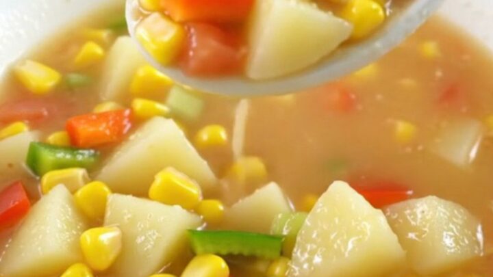 A top-down view of a creamy Cajun corn chowder in a slow cooker insert on a granite countertop.