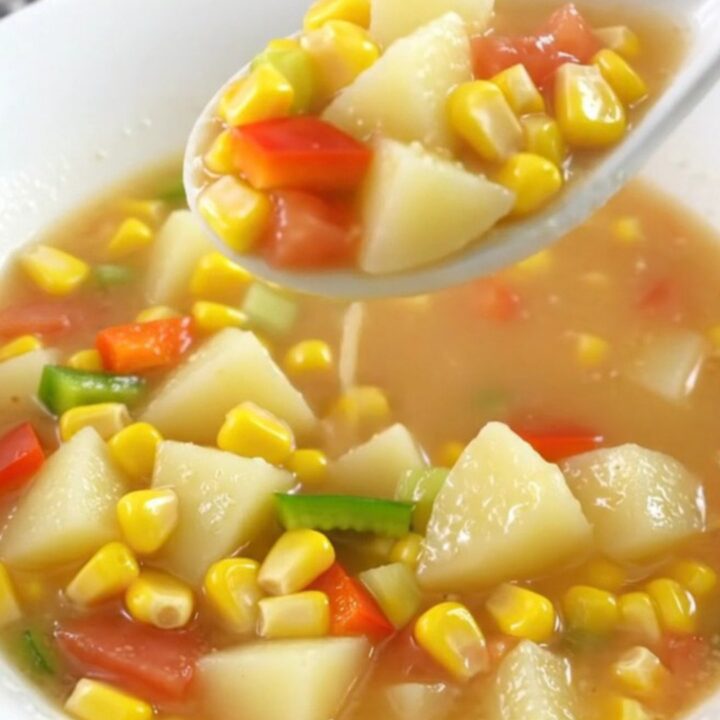 A top-down view of a creamy Cajun corn chowder in a slow cooker insert on a granite countertop.