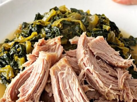 A close-up of a slow-cooked pork roast with collard greens in a black ceramic slow cooker insert.