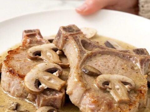 A close-up of tender boneless pork chops smothered in a creamy mushroom and ranch sauce, served on a white plate.