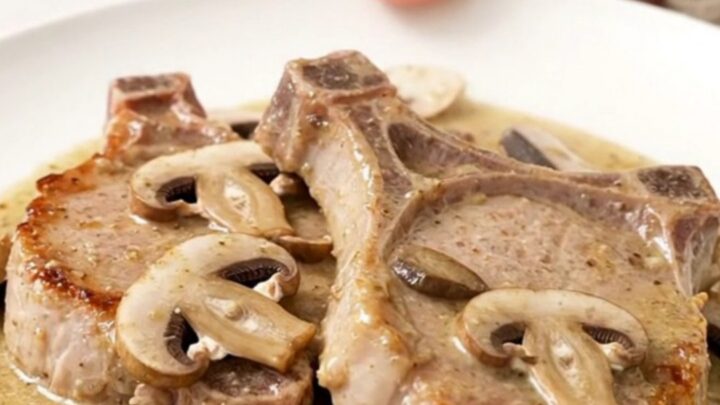 A close-up of tender boneless pork chops smothered in a creamy mushroom and ranch sauce, served on a white plate.
