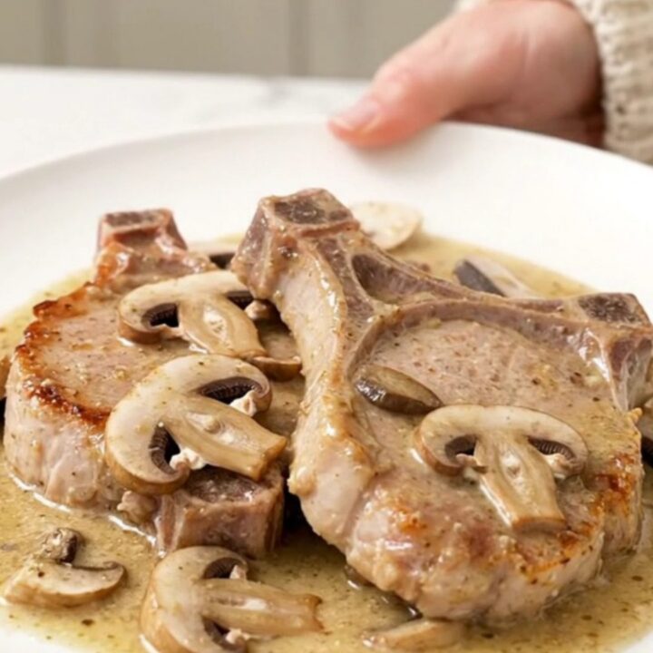 A close-up of tender boneless pork chops smothered in a creamy mushroom and ranch sauce, served on a white plate.
