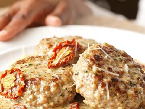 Close-up of slow-cooked turkey burger steaks covered in a creamy parmesan sauce with sun-dried tomatoes.