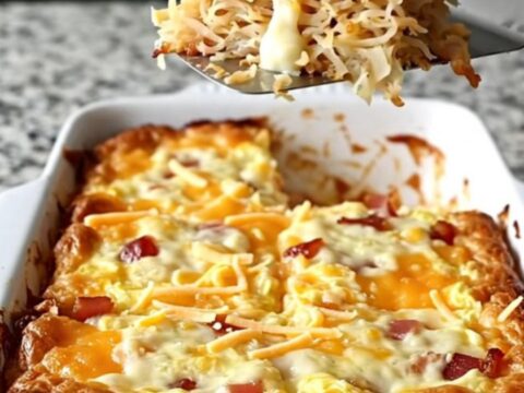 A golden, bubbling Amish bacon and hash brown breakfast casserole in a white rectangular dish.