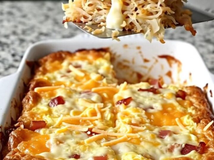 A golden, bubbling Amish bacon and hash brown breakfast casserole in a white rectangular dish.