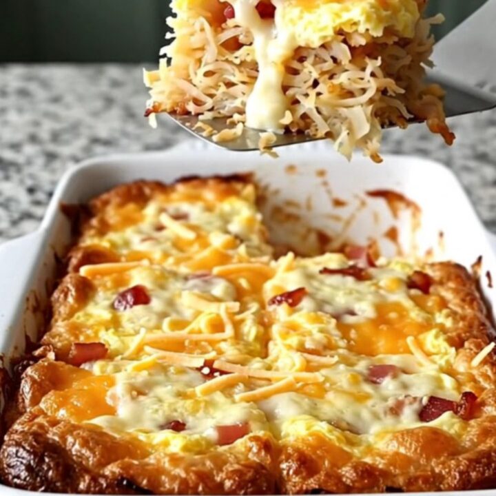 A golden, bubbling Amish bacon and hash brown breakfast casserole in a white rectangular dish.