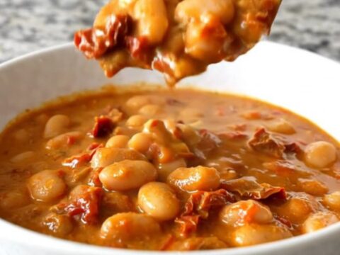 A shallow white bowl filled with creamy butter beans and sun-dried tomatoes in a rich sauce.