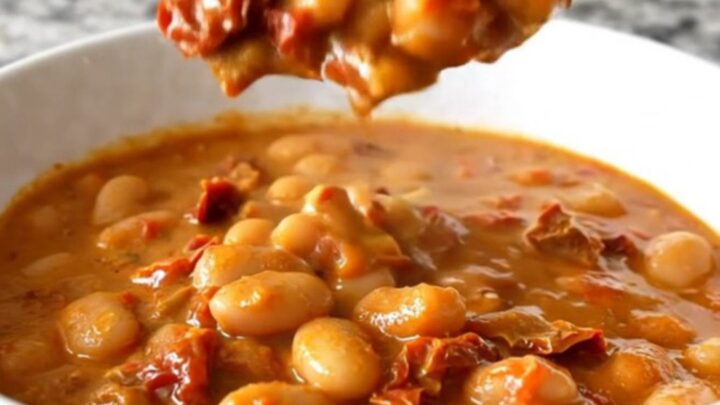 A shallow white bowl filled with creamy butter beans and sun-dried tomatoes in a rich sauce.