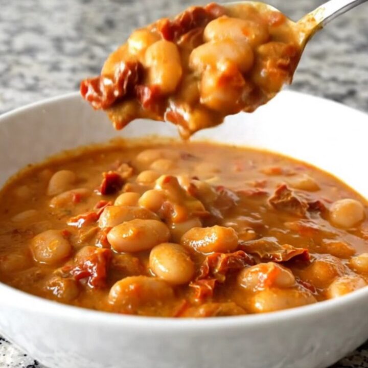 A shallow white bowl filled with creamy butter beans and sun-dried tomatoes in a rich sauce.