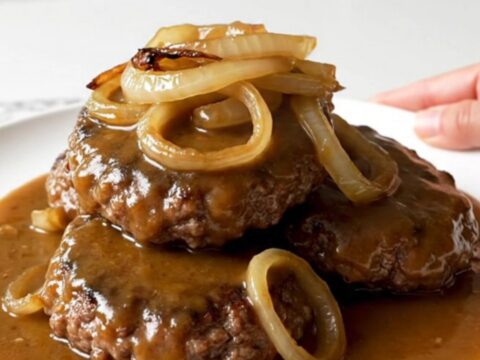 A close-up of tender hamburger steaks covered in caramelized onions and rich brown gravy in a slow cooker.