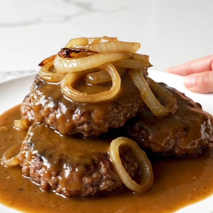 A close-up of tender hamburger steaks covered in caramelized onions and rich brown gravy in a slow cooker.