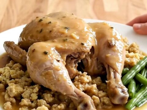 A white oval slow cooker filled with cooked chicken breasts, green beans, and herb stuffing in gravy.
