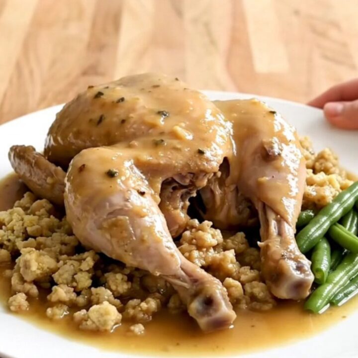 A white oval slow cooker filled with cooked chicken breasts, green beans, and herb stuffing in gravy.