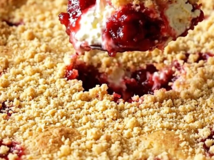 A warm cherry cheesecake dump cake in a white baking dish with a golden crumbly top.