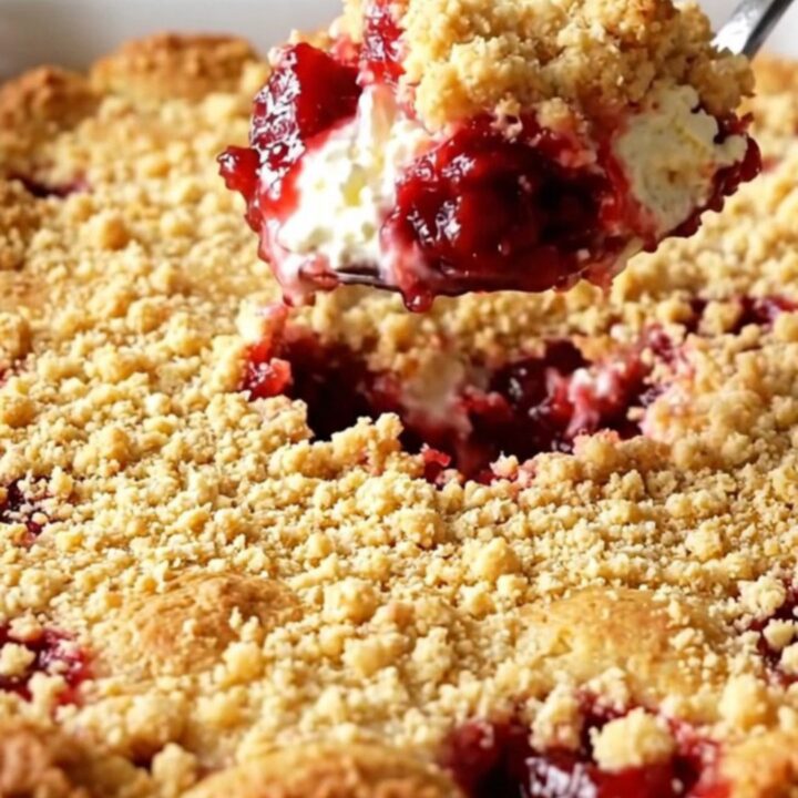 A warm cherry cheesecake dump cake in a white baking dish with a golden crumbly top.