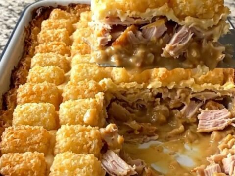 A golden, bubbling French onion turkey potato tot casserole in a white baking dish.