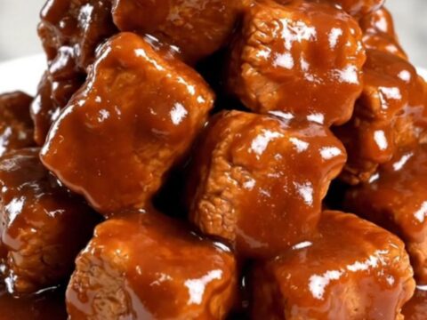 A close-up of tender, saucy pork burnt ends in a slow cooker, featuring a rich, dark glaze and visible spice rub.